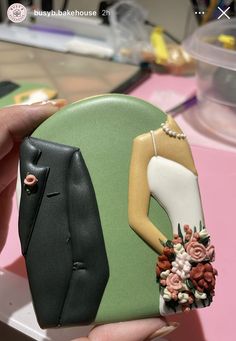 a hand holding a cake shaped like a woman's dress and jacket with flowers on it