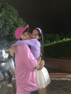 a man in a pink shirt and white skirt kissing a woman wearing a pink hat