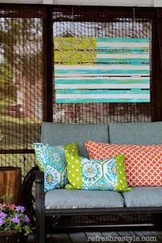 a couch with colorful pillows on it sitting in front of a screen door and window