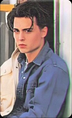 a young man with black hair sitting in front of a wall