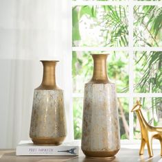 two gold vases sitting on top of a table next to a book and giraffe statue