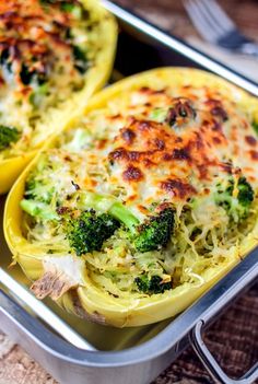 two stuffed peppers with broccoli and cheese in a metal pan on a table