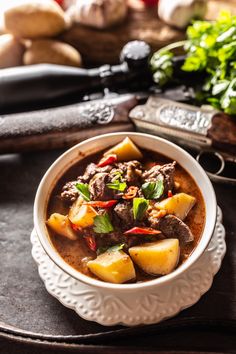 a white bowl filled with meat and potatoes on top of a wooden tray next to other vegetables