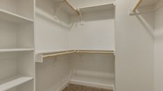 an empty walk in closet with white walls and shelving units on each side, along with carpeted flooring