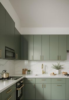 a kitchen with green cabinets and white counter tops, gold pulls on the door knobs