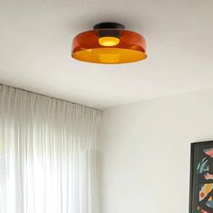 an orange light hanging from the ceiling above a bed in a room with white curtains