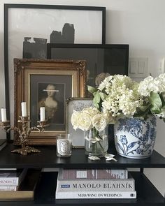 a black table topped with books and vases filled with flowers next to framed pictures