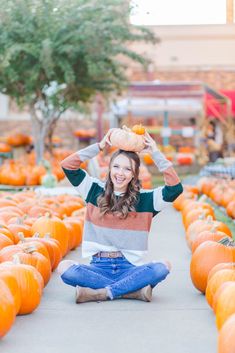 a woman sitting on the ground with pumpkins in front of her and smiling at the camera