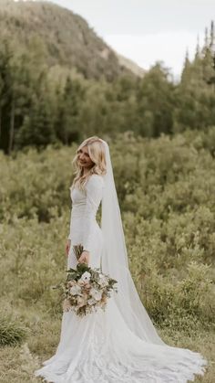 a woman in a wedding dress standing in the grass with her veil over her head