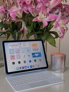 a laptop computer sitting on top of a desk next to a vase filled with flowers