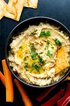 hummus in a bowl with tortilla chips and carrots on the side