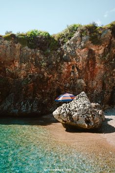 an umbrella sitting on top of a rock next to the ocean near some rocks and water