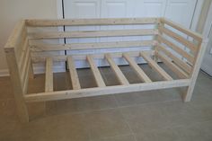 a wooden bed frame sitting on top of a tile floor next to a white door