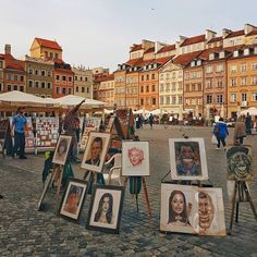 many paintings are on display in front of some buildings and people walking down the street