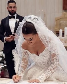 a woman in a wedding dress signing the register at a table with a man standing behind her