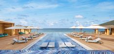 an outdoor pool with chaise lounges and umbrellas on the deck overlooking the ocean