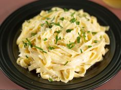 a black plate topped with pasta and garnished with parsley on the side