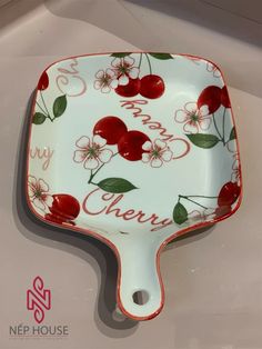 a red and white plate with cherries painted on it's sides, sitting on a table