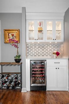 a wine cooler in the middle of a kitchen with white cabinets and wood floors,