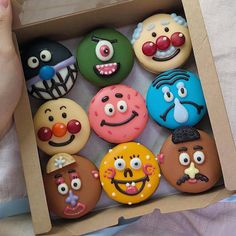 a box filled with lots of different colored cupcakes covered in icing and decorated like cartoon faces