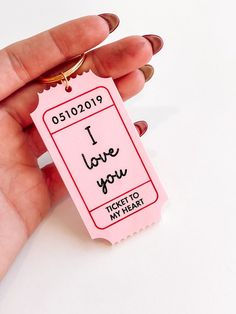 a hand holding a pink ticket with the words i love you written in black ink