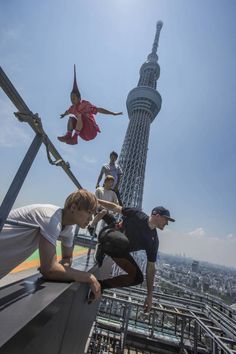 some people are standing on the edge of a building and one person is jumping in the air