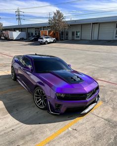 a purple camaro is parked in an empty parking lot next to a building with two cars behind it