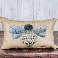 a small pillow with a blue and white bee design on the front, sitting on top of a wooden table