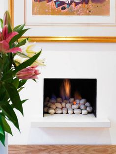 a white fireplace with rocks in it next to a potted plant and framed artwork