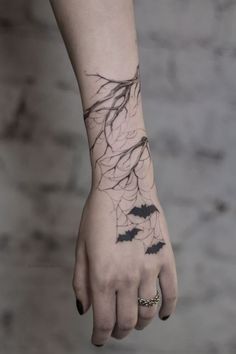 a woman's arm with black ink on it and bats in the branches behind her