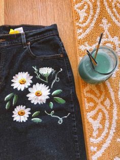 a pair of jeans with daisies painted on them next to a cup and strawberries