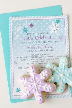 two decorated cookies sitting on top of a blue and white card with snowflakes