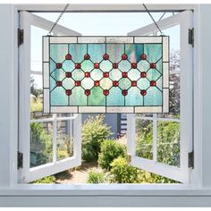 a stained glass window hanging from the side of a house with an open door and garden behind it