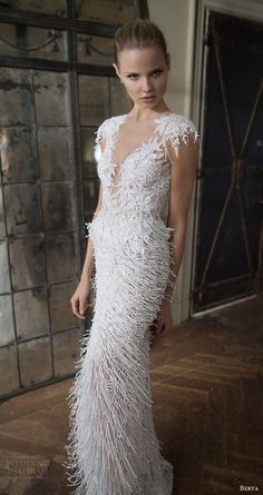 a woman standing in front of a mirror wearing a white dress with feathers on it