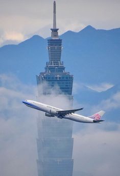 an airplane flying in front of a tall building with a sky scraper behind it