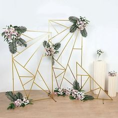 three gold geometric frames with flowers and greenery on the sides, against a white wall