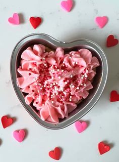 a heart shaped tin with pink frosting and sprinkles on it, surrounded by hearts