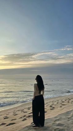 a woman sitting on top of a sandy beach next to the ocean