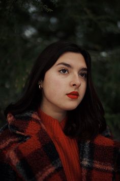 a woman with dark hair wearing a red sweater and black and white checkered coat