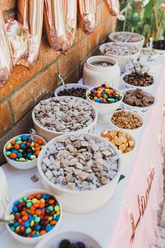 a table topped with lots of bowls filled with food next to a brick wall covered in candy