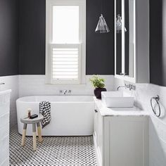 a white bath tub sitting under a bathroom window next to a sink and shower stall