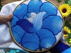 a person holding a blue flower in front of some yellow and white flowers on a table