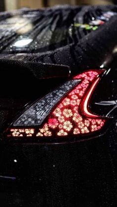 the rear end of a black sports car with red flowers on it's tail lights