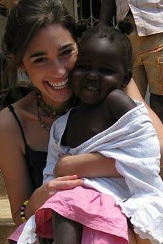 a woman holding a small child in her arms and smiling at the camera with other people behind her