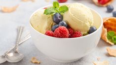 two scoops of ice cream with raspberries and blueberries in a white bowl