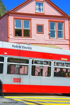 a red and white bus is parked in front of a pink building with two windows