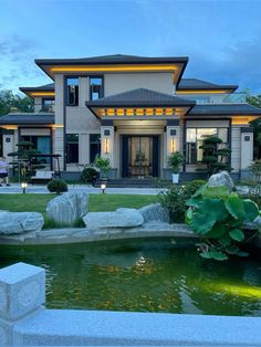 a large house with a pond in the front yard and landscaping around it at dusk