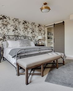 a bedroom with a large bed and floral wallpaper on the walls, along with a bench