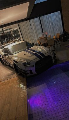 a white sports car parked in front of a living room with purple lighting on the floor