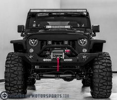 the front end of a black jeep with its lights on and four wheel drive tires